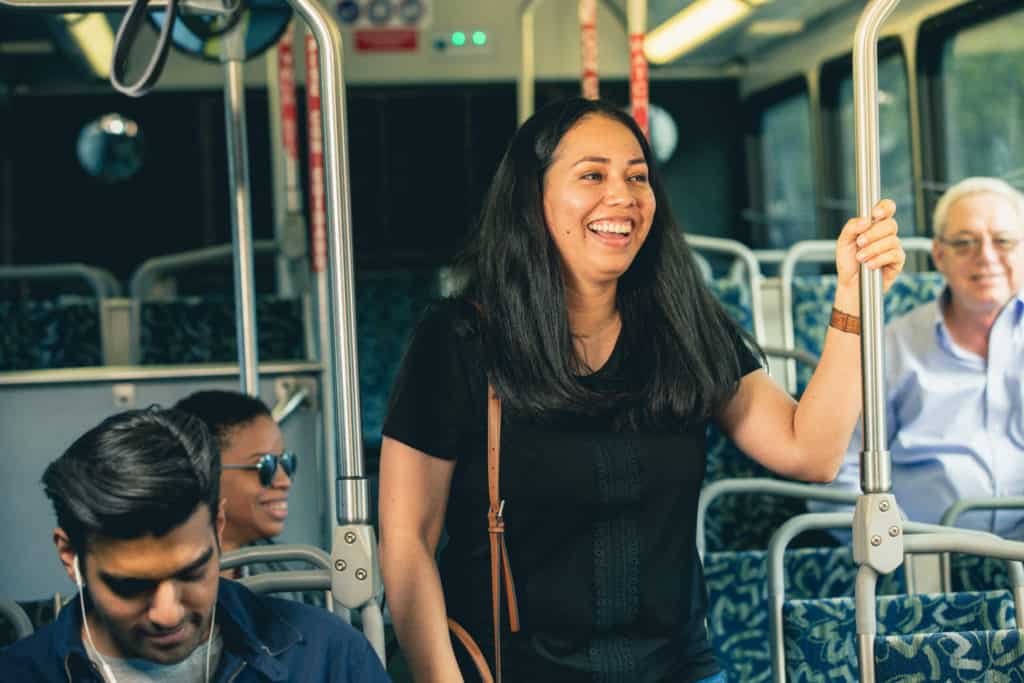 Woman on bus standing with purse smiling with several others close